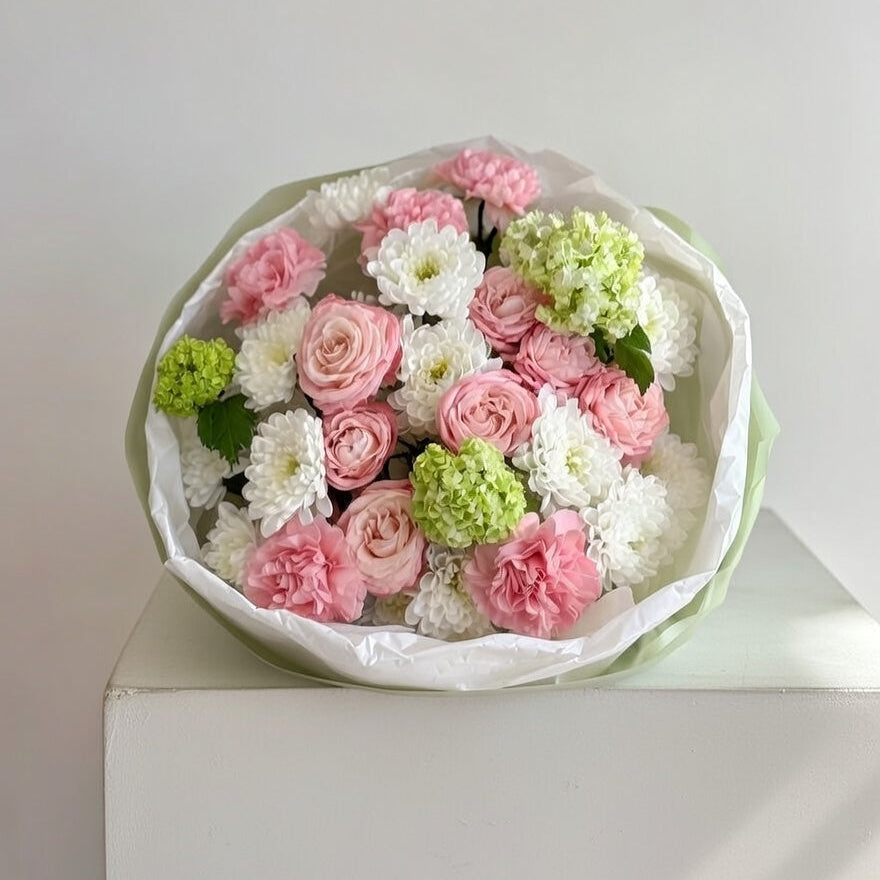 Bouquet of pink, white, and green flowers in a white box on a light gray background