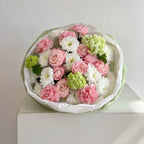 Bouquet of pink, white, and green flowers in a white box on a light gray background