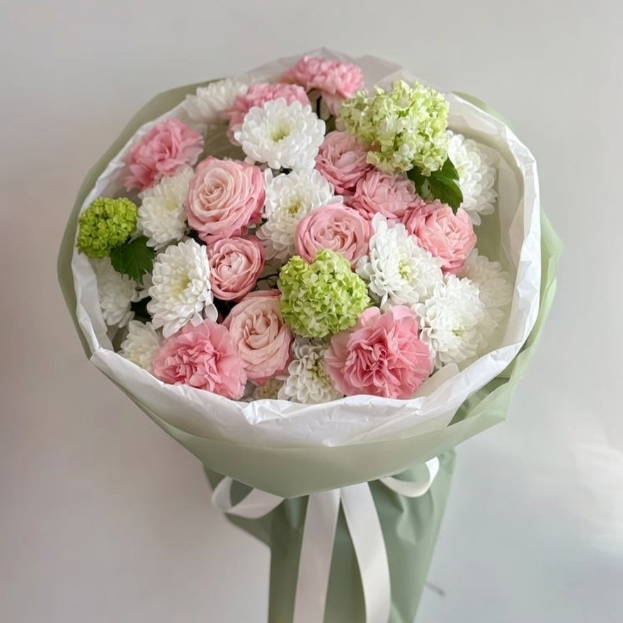Bouquet of pink, white, and green flowers wrapped in paper with a ribbon on a light gray background