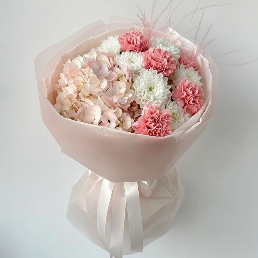 Bouquet of pink and white flowers wrapped in pink paper with ribbons on a light gray background