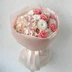 Bouquet of pink and white flowers wrapped in pink paper with ribbons on a light gray background