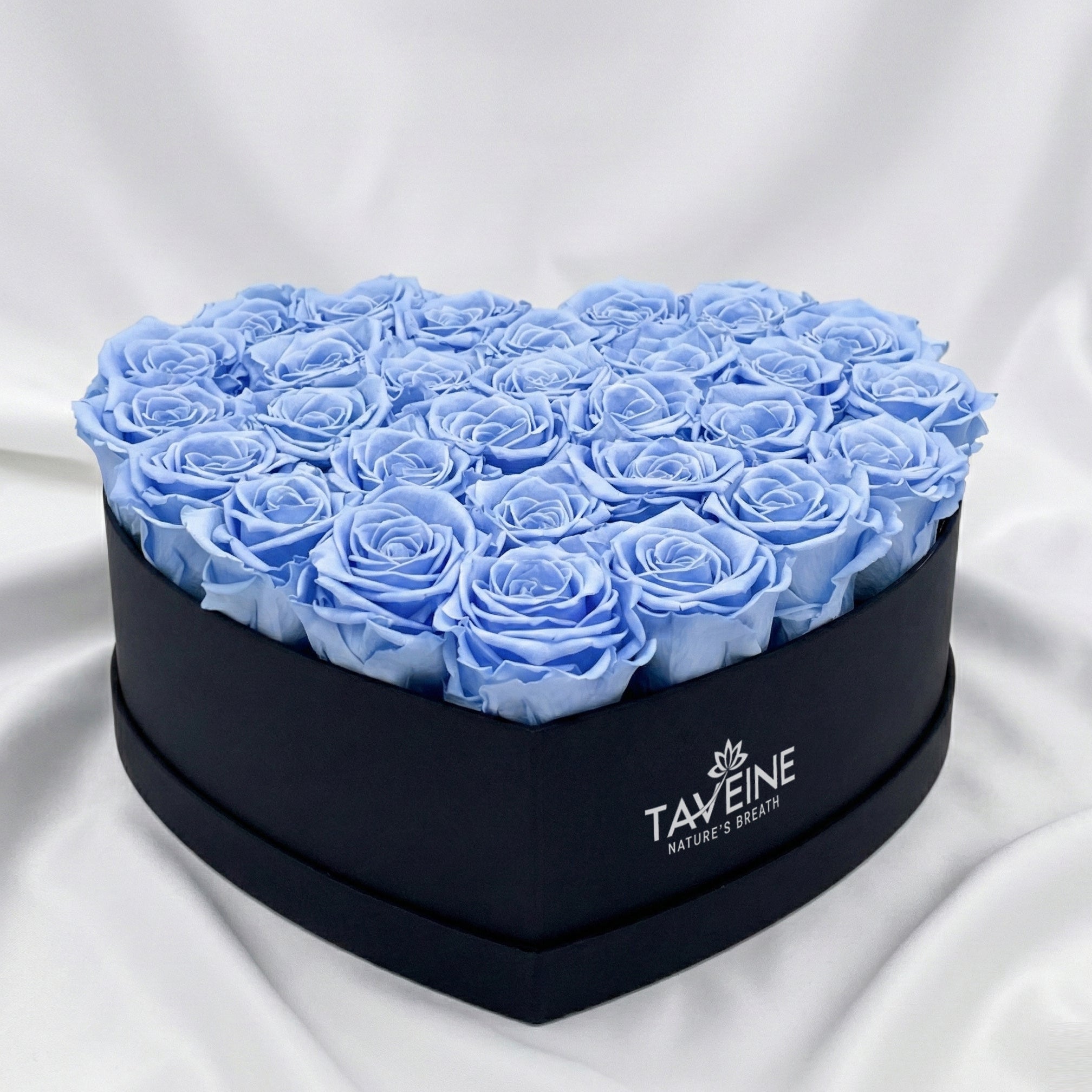 Heart-shaped box filled with blue roses on a white fabric background