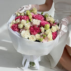 Bouquet of pink and white flowers held by a person in a white dress and gloves on a light background