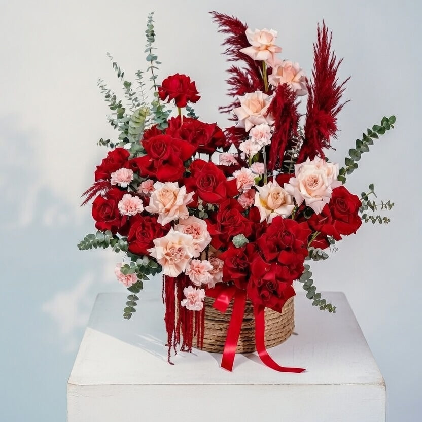 Bouquet of red and pink flowers with pampas grass on a white pedestal against a light gray background