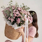 Woman holding a large bouquet of flowers in a wicker basket against a plain background