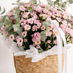 Bouquet of pink flowers in a woven basket with a white ribbon on a light background